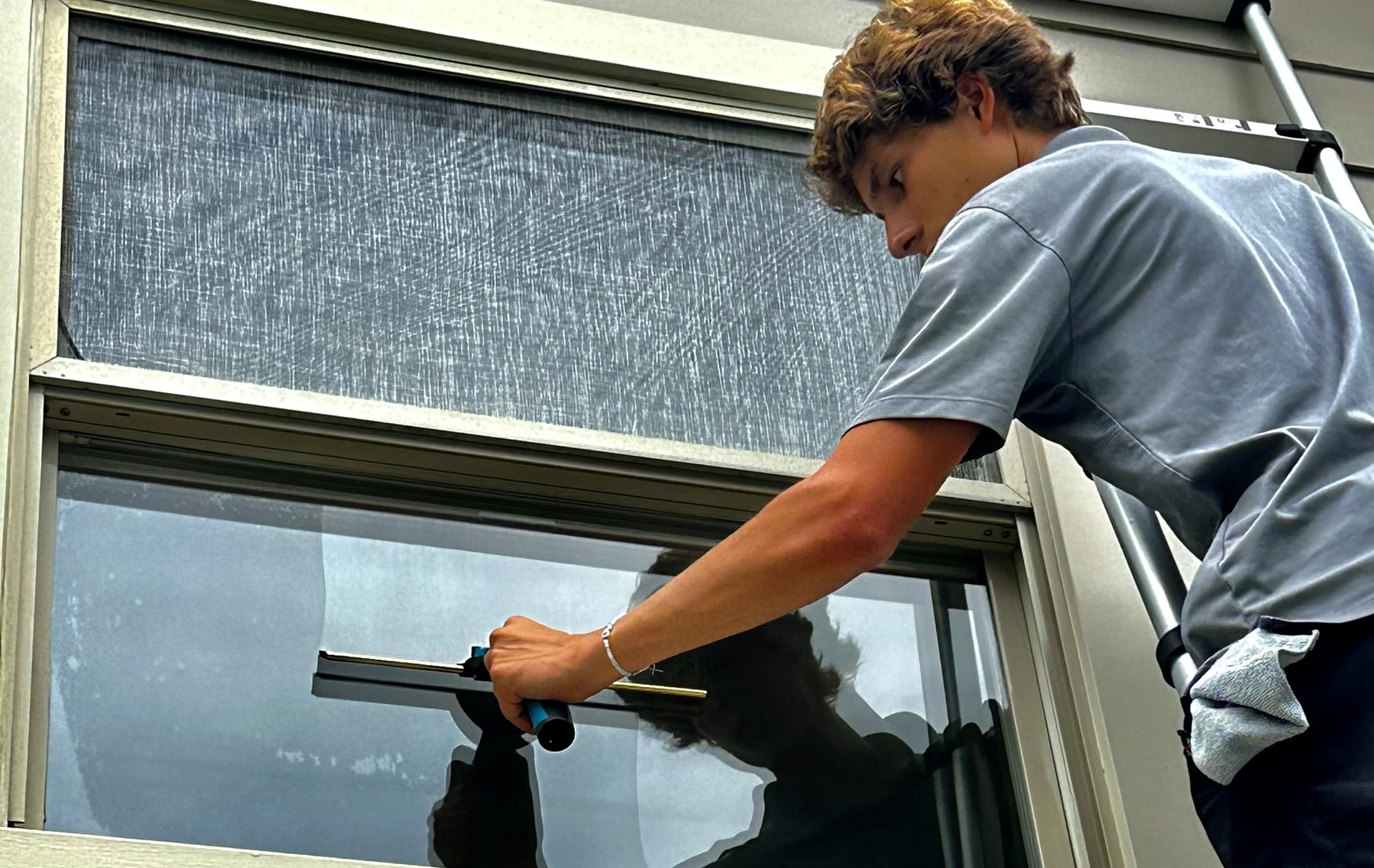 A Clearwater Window Care technician squeegeeing a window from a ladder
